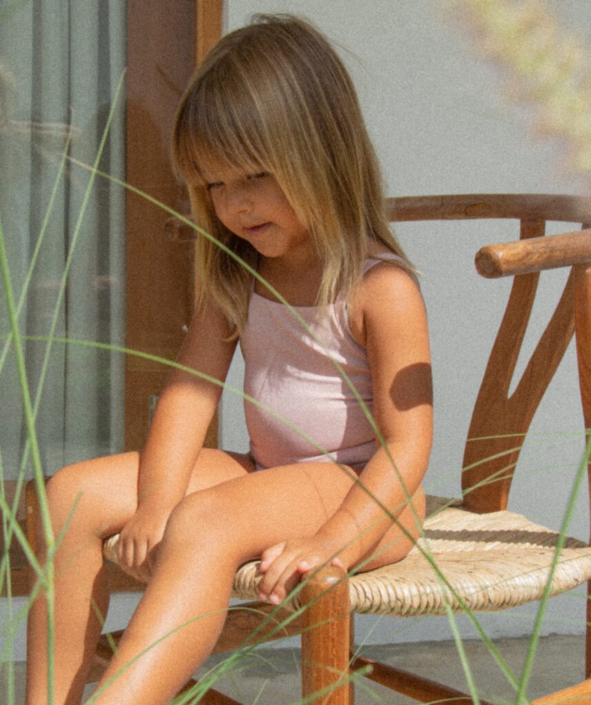 A little girl wearing sustainable swimwear sitting on a wooden chair.