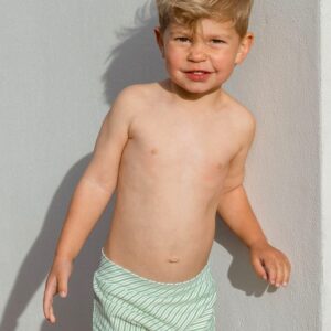 A young boy in Retro Wave By Ina - Lumi Short Swim Nappy swim trunks leaning against a wall.