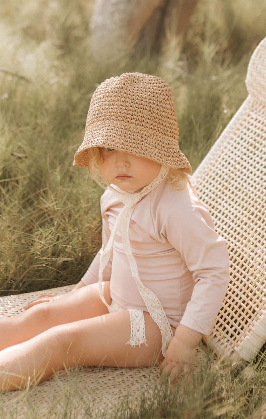 A baby is sitting on a wicker chair in the sustainable swimwear.
